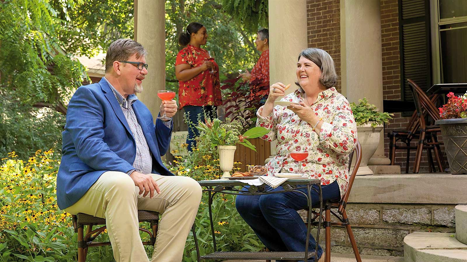 Chris and Ouita Michel sit together at a patio table outside their Holly Hill Inn restaurant with cocktails and plates of crackers.